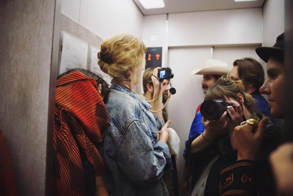A group crowded into an elevator while two people take photos with cameras.